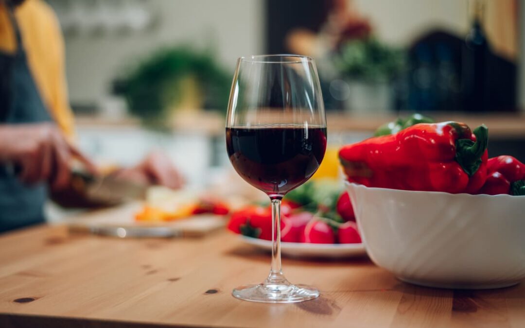 Red wine in a glass standing on a kitchen counter with food behind